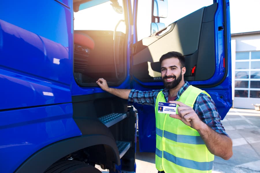 Successful CDL candidate smiles standing next to blue truck, holding new license in hand