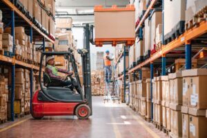 Uniformed worker driving forklift and loading boxes into warehouse